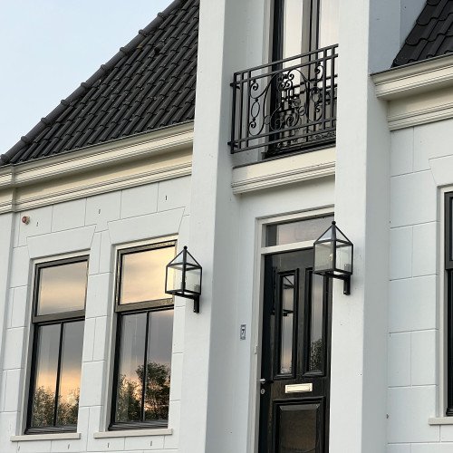 buitenlamp zwart met een rvs zwart frame aan wandsteun met heldere beglazing, lichtbron is zichtbaar, huisjes model vormgeving